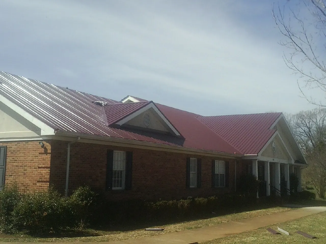 Red metal roof with gabled entries on a long brick building, from a Hail Damage Roof Repair job in Cornish