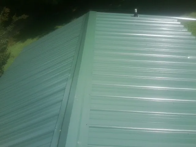 New green metal panels meeting at the ridge of a roof — Flat Roof Repair work by our crew in Cornish
