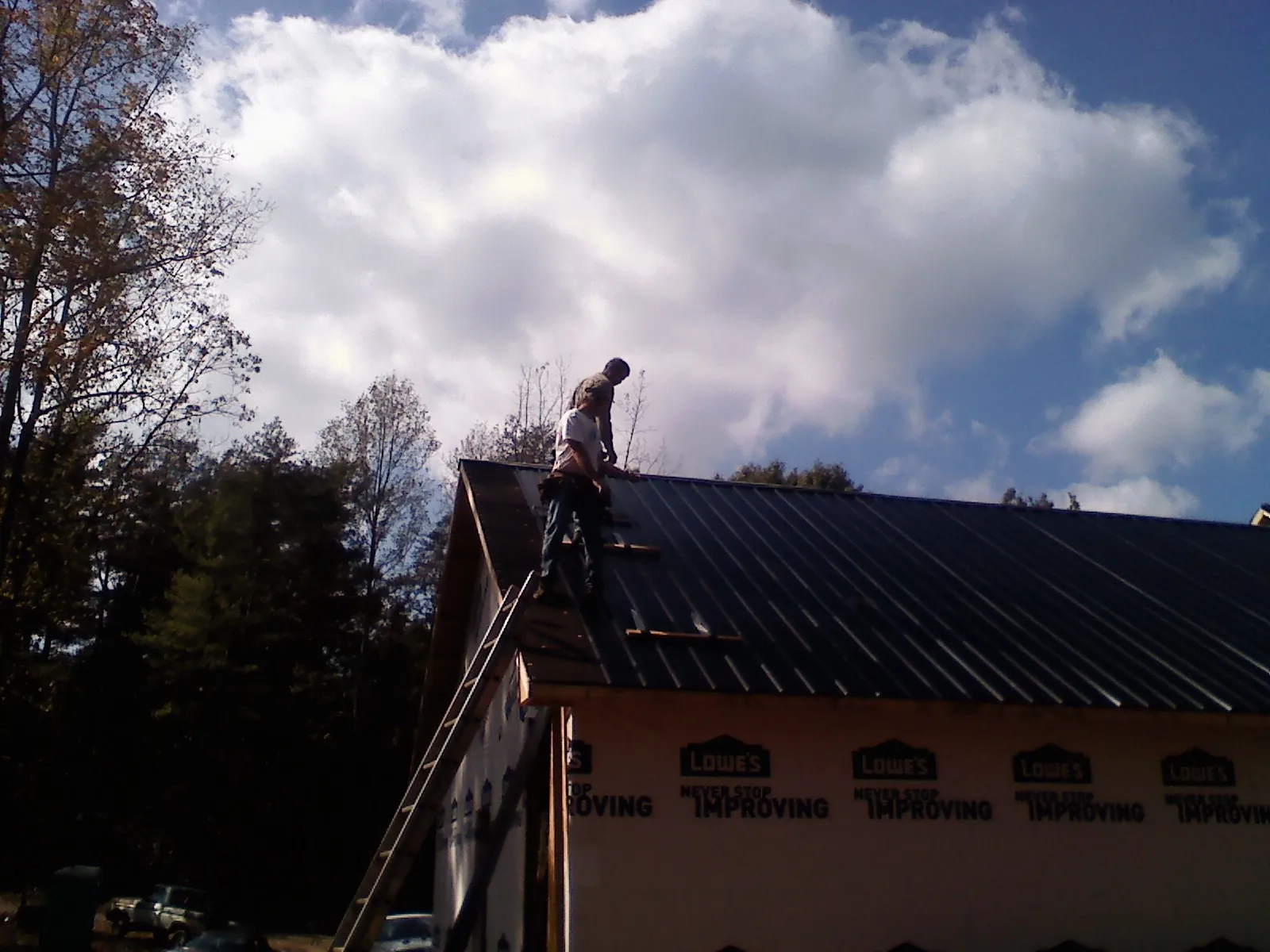 Roofer fastening dark metal panels high against a cloudy sky, from a Roof Inspection job in Cornish
