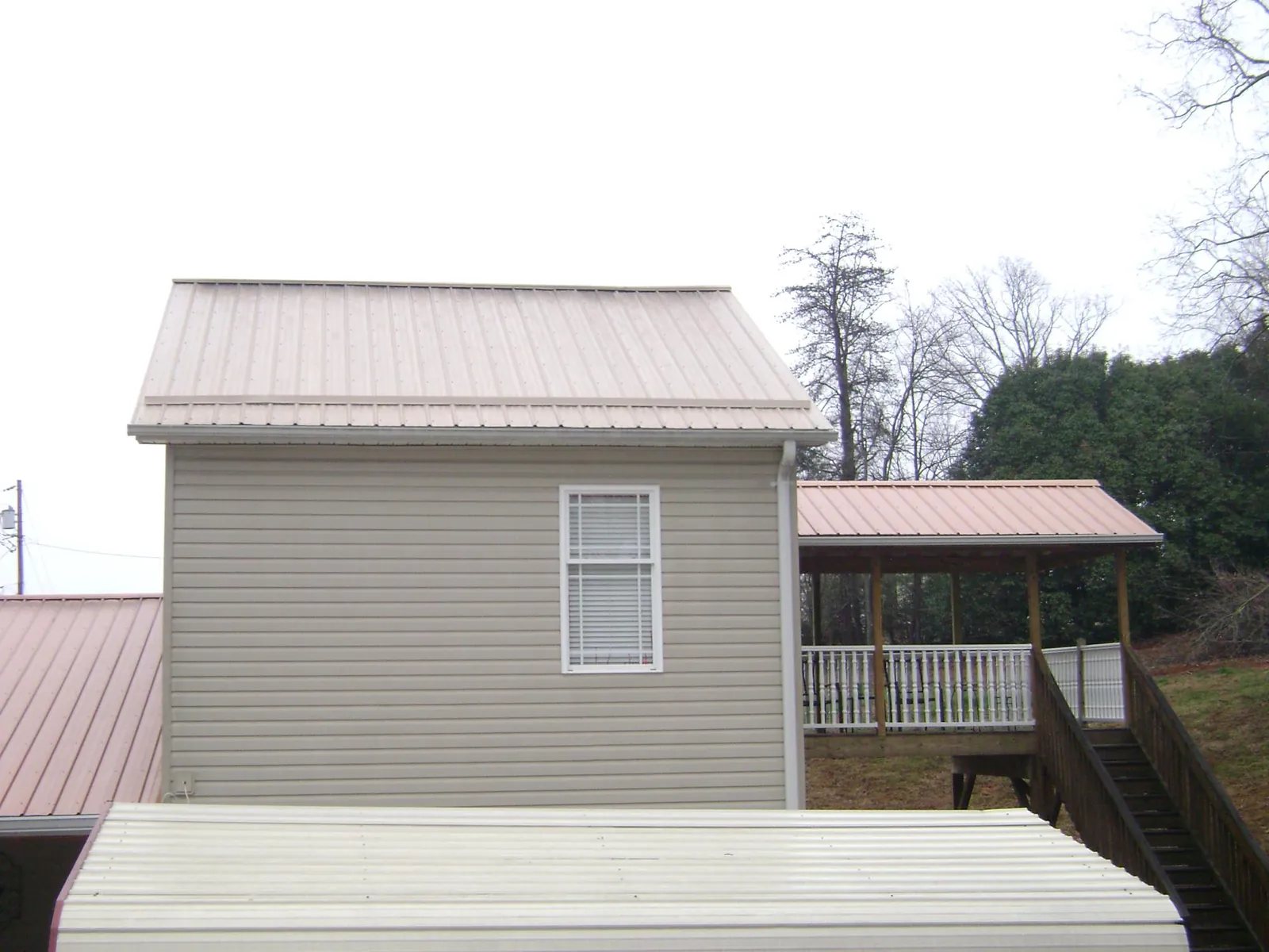 Tan metal roofs on a two story addition and attached porch, from a Roof Replacement job in Cornish