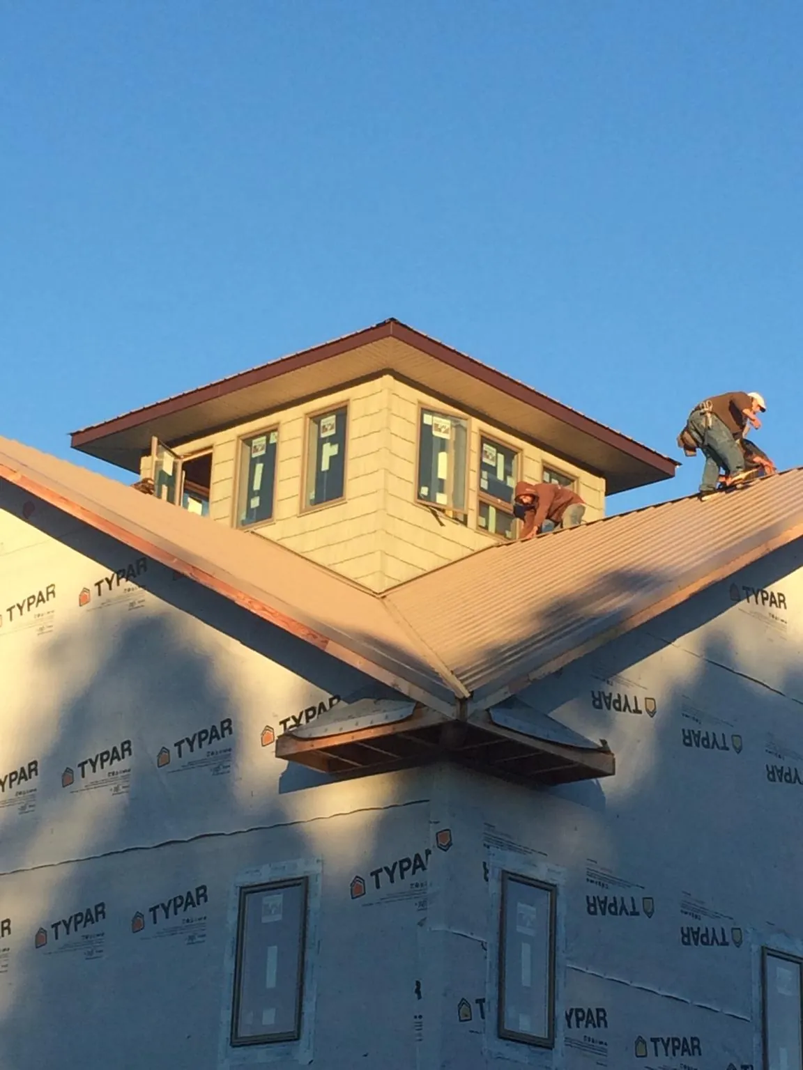 Roofers working around a rooftop cupola on a new metal roof at sunset — Roof Waterproofing in Cornish by Roofing Brothers